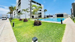 A modern building with a swimming pool, surrounded by well-maintained grass and palm trees.