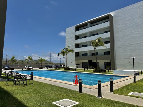 Un edificio moderno con piscina, mobiliario exterior y palmeras.