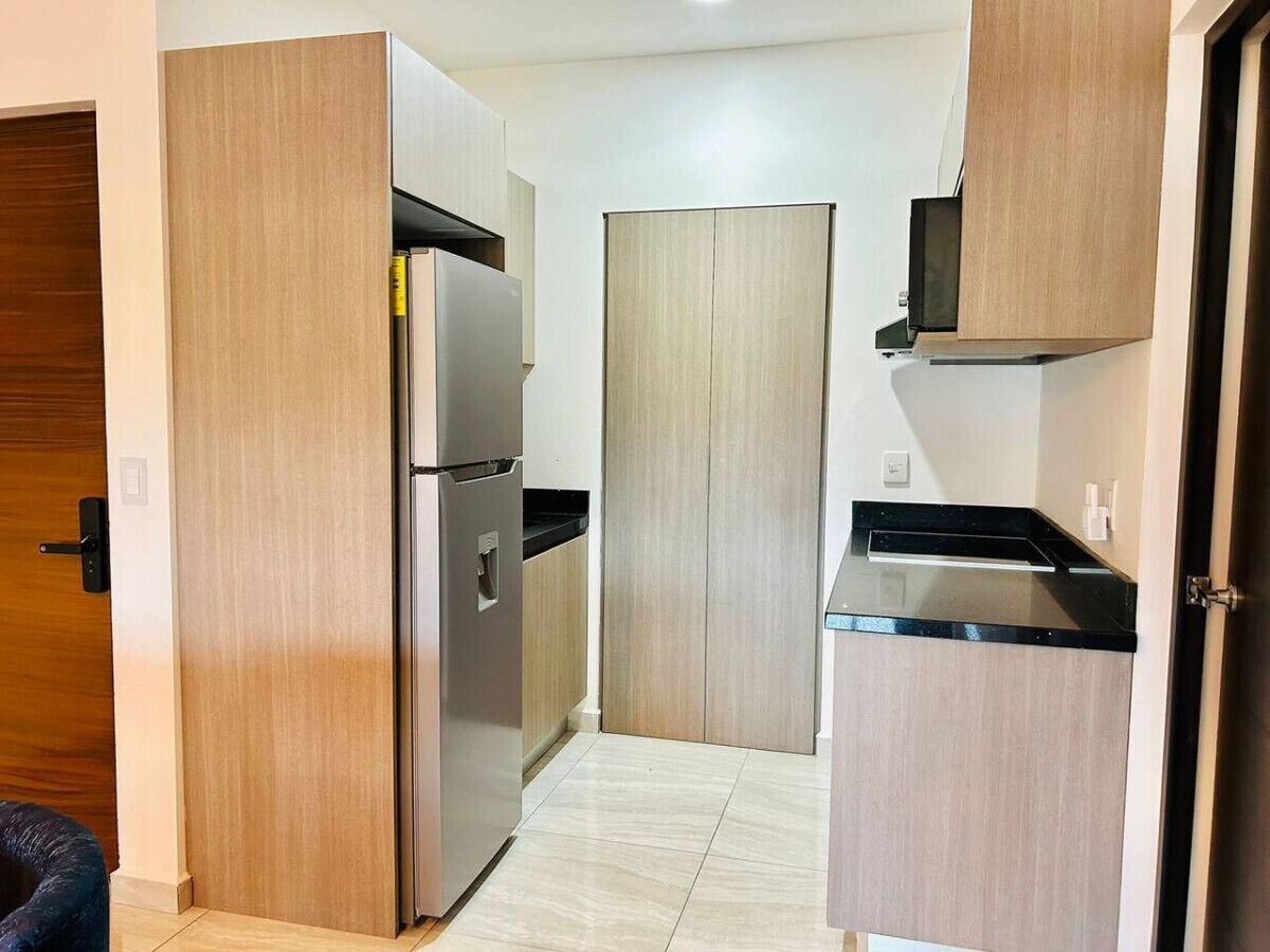 Una cocina funcional con armarios de madera, un refrigerador de acero inoxidable y una encimera negra.