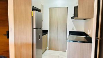 Una cocina funcional con armarios de madera, un refrigerador de acero inoxidable y una encimera negra.