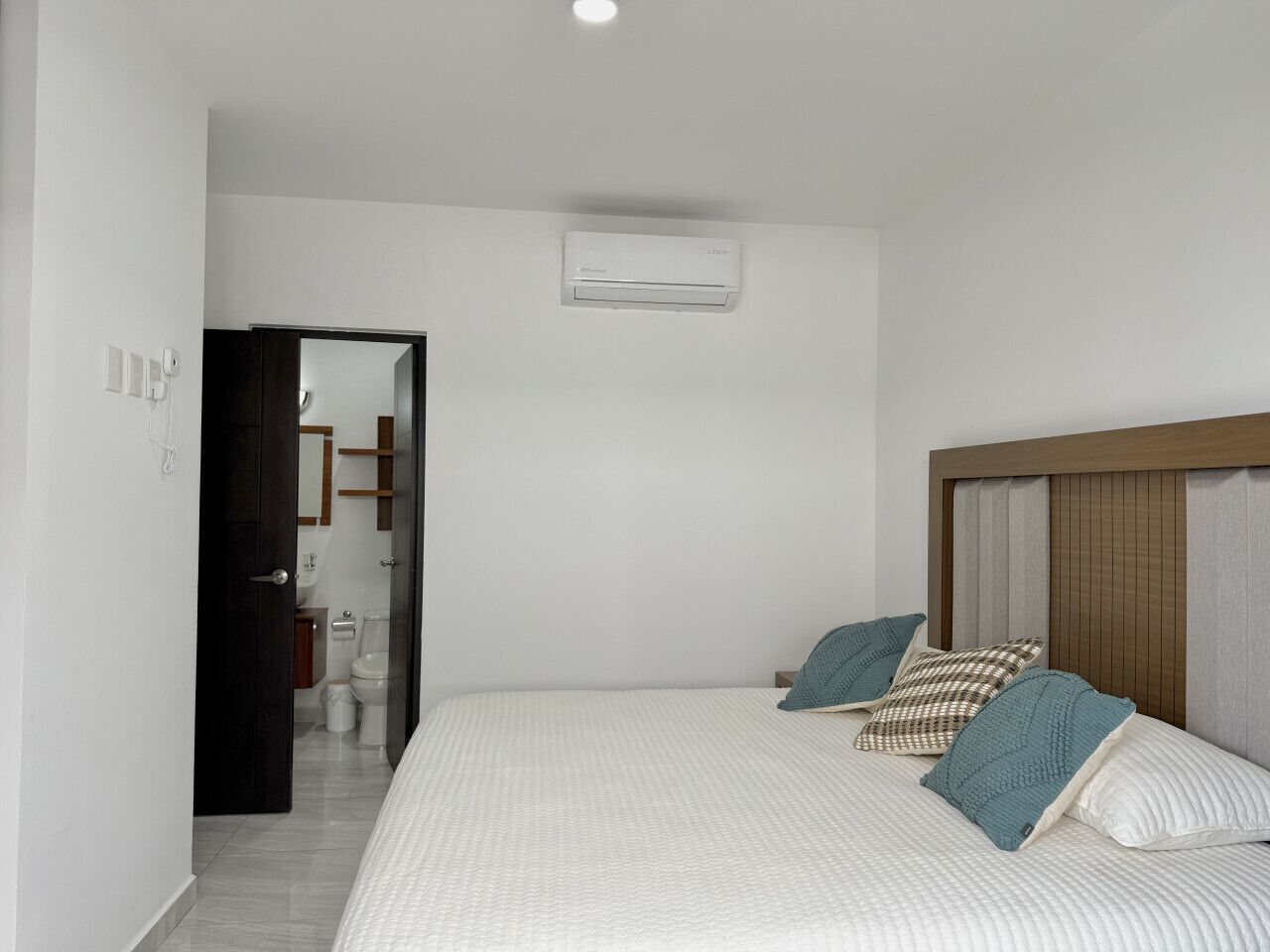 Un dormitorio con cama, almohadas, cabecera de madera y un equipo de aire acondicionado en la pared.