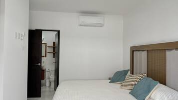 Un dormitorio con cama, almohadas, cabecera de madera y un equipo de aire acondicionado en la pared.