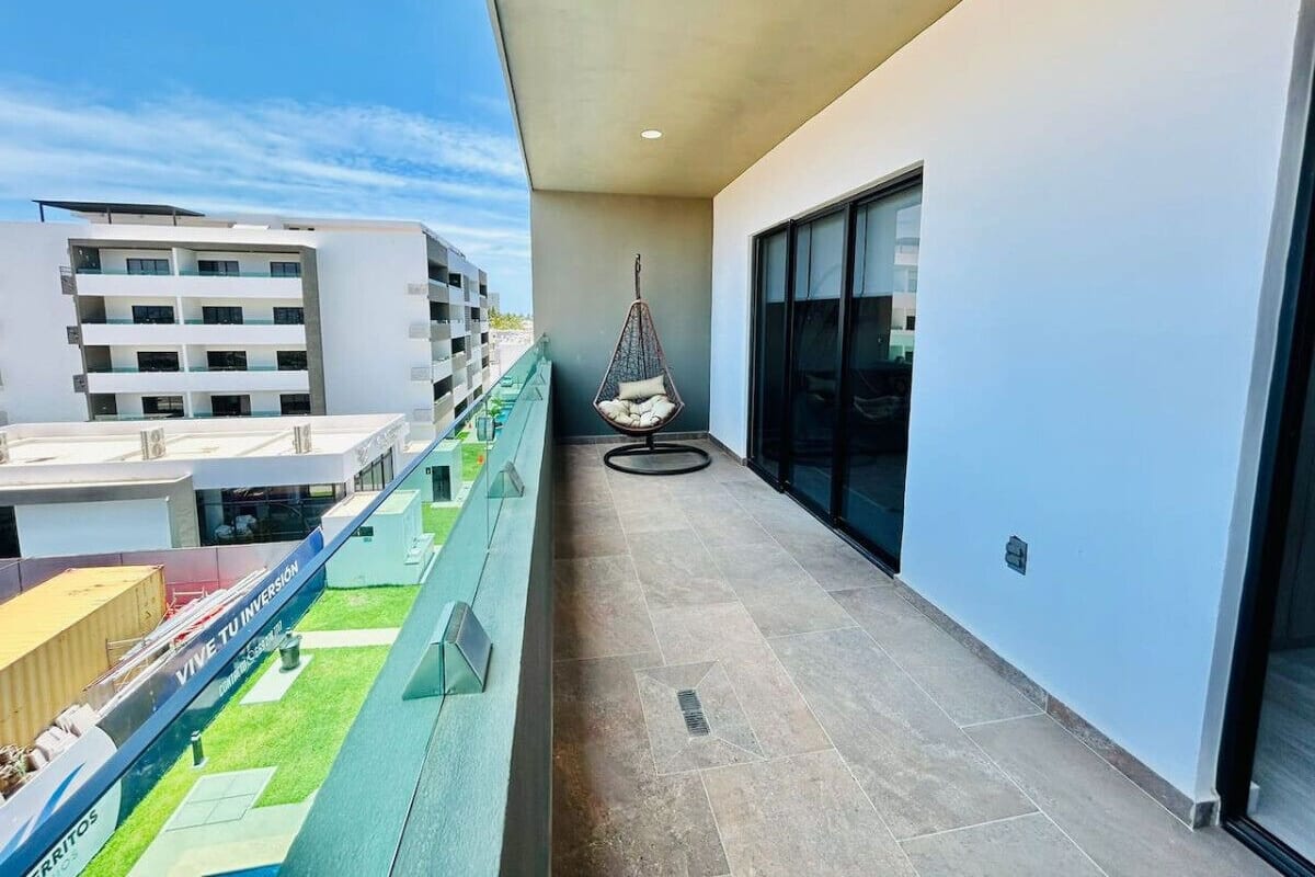 A balcony with a hanging chair, a glass railing, and a view of other buildings.
