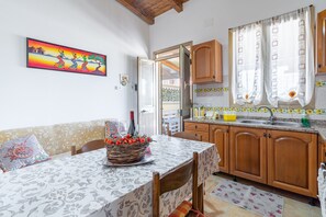 A kitchen with wooden cabinets, a dining table with a patterned tablecloth, and a basket of fruit.
