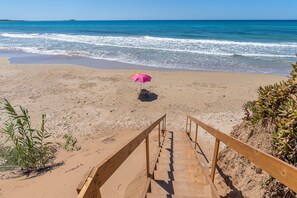 A beach with a wooden staircase leading to a sandy area with an umbrella.