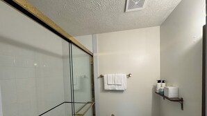 A bathroom with a glass shower enclosure, a toilet, a towel rack with towels, and a shelf with toiletries. - Waterfall Cottage at GOTL (Geneva)