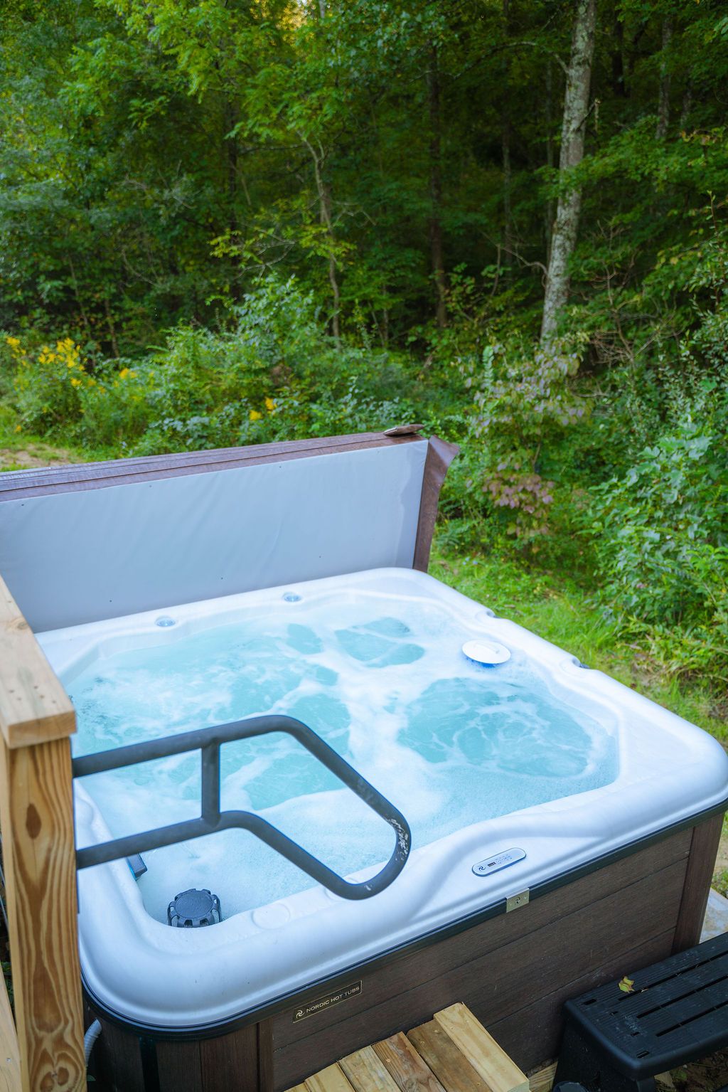 A hot tub with a wooden deck and a metal safety rail.