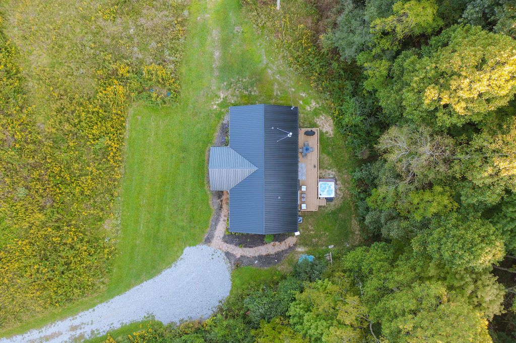 An aerial view of a house with a sloped roof, surrounded by dense greenery and a small pond.