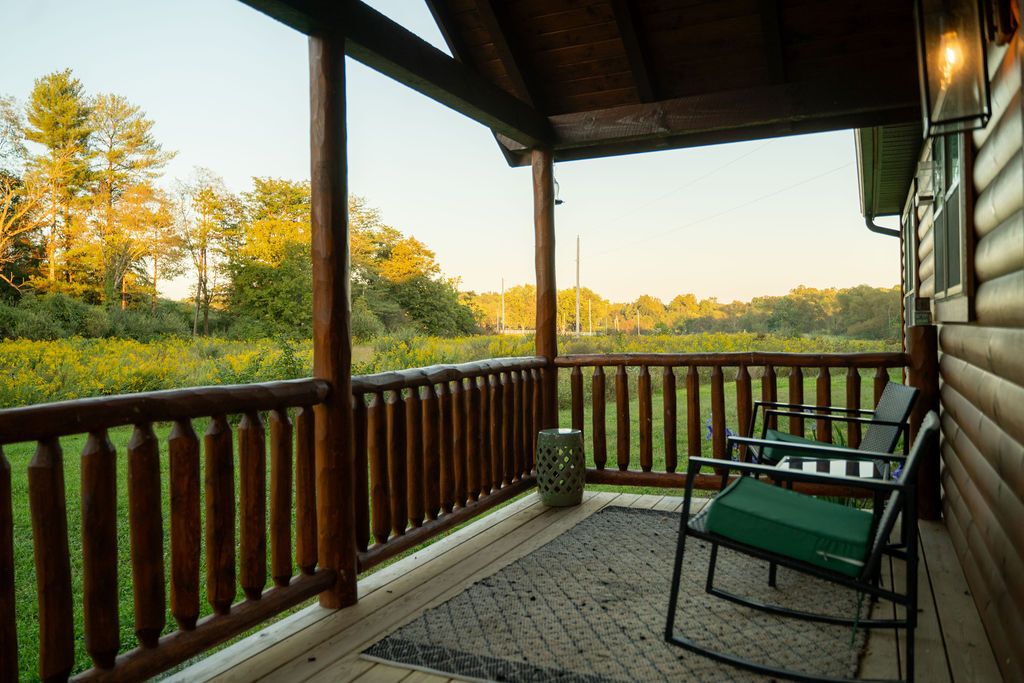 A covered porch with a wooden railing, a green cushioned chair, and a small table.