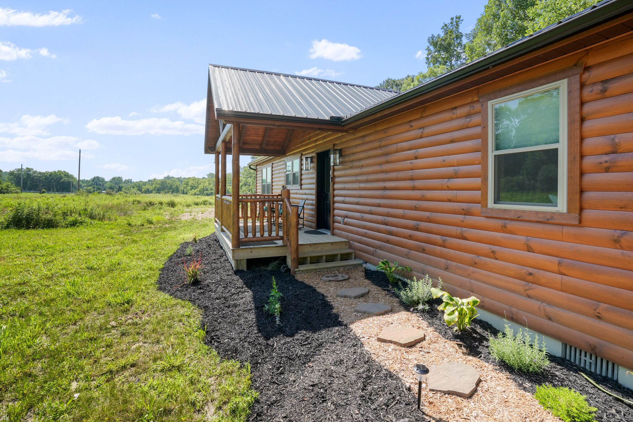 A log cabin with a porch, a small garden, and a clear sky.