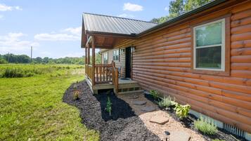 A log cabin with a porch, a small garden, and a clear sky.