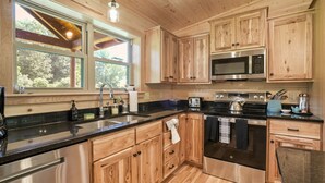 A modern kitchen with wooden cabinets, stainless steel appliances, and a large window providing natural light. - Coyote Creek | Hocking Hills, 40 Acre Retreat (McArthur)