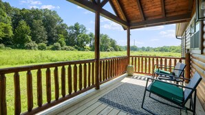 A wooden deck with a railing, outdoor furniture, and a view of a green field and trees. - Coyote Creek | Hocking Hills, 40 Acre Retreat (McArthur)