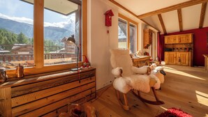 Una habitación acogedora con muebles de madera, un sillón mecedora y vistas a las montañas a través de amplios ventanales.