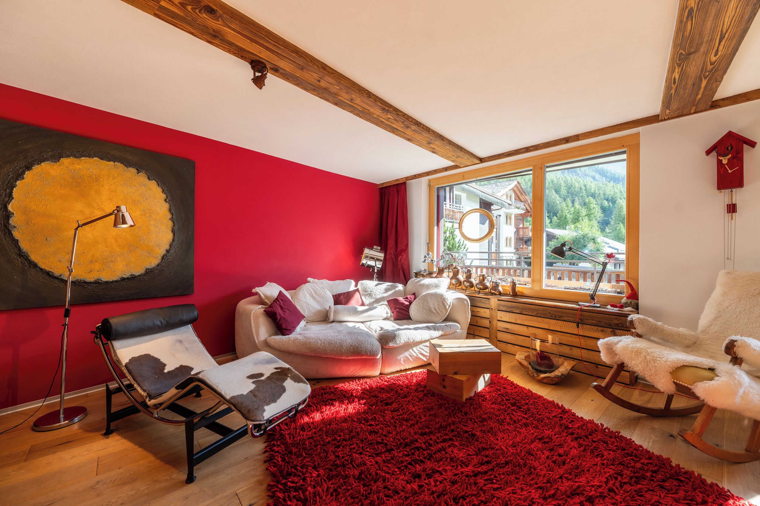 A cozy living room with a red wall, a large window, a rocking chair, and a modern floor lamp.