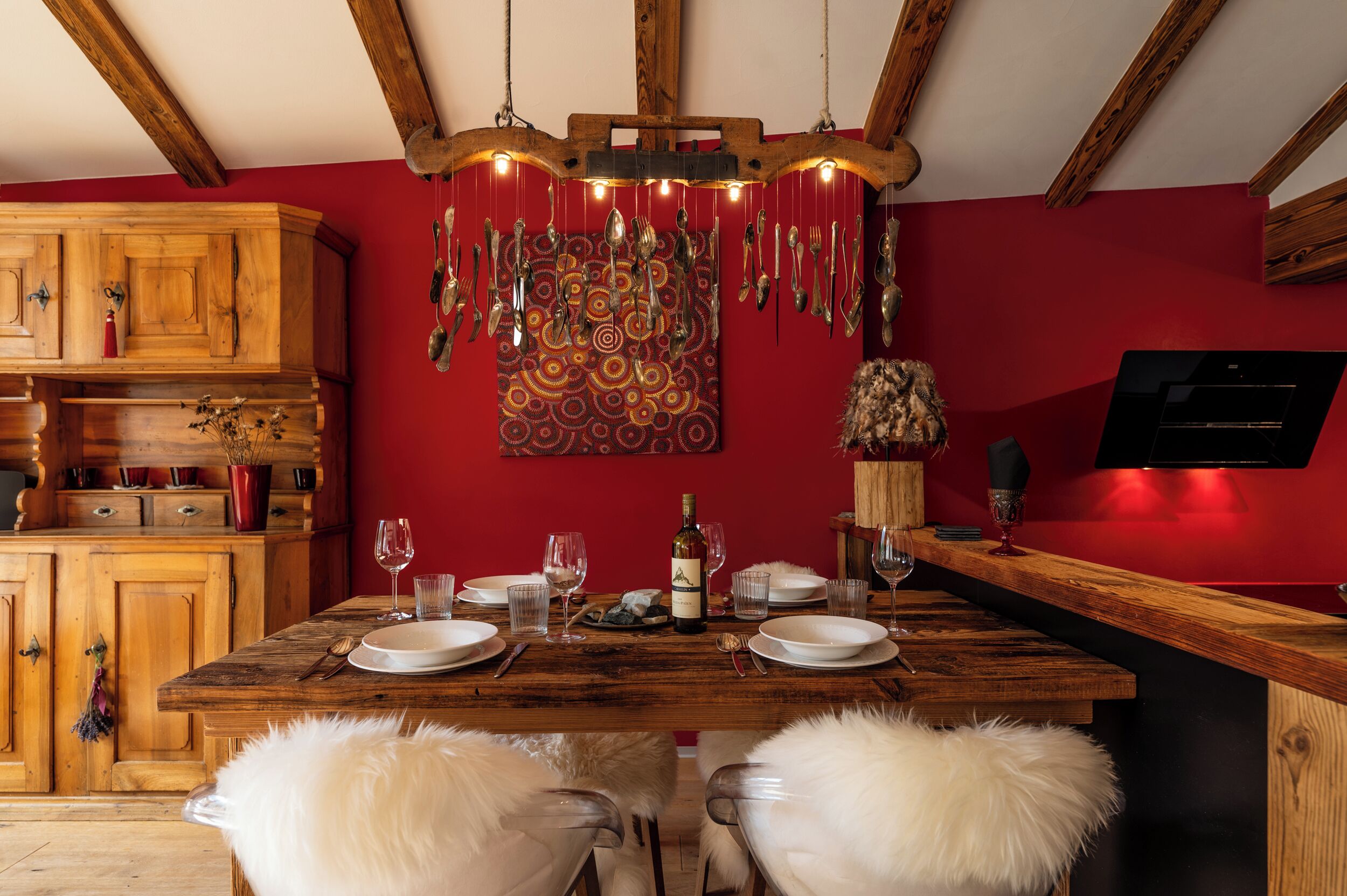 A wooden dining table set with plates, glasses, and cutlery, a wine bottle, and a hanging light fixture.