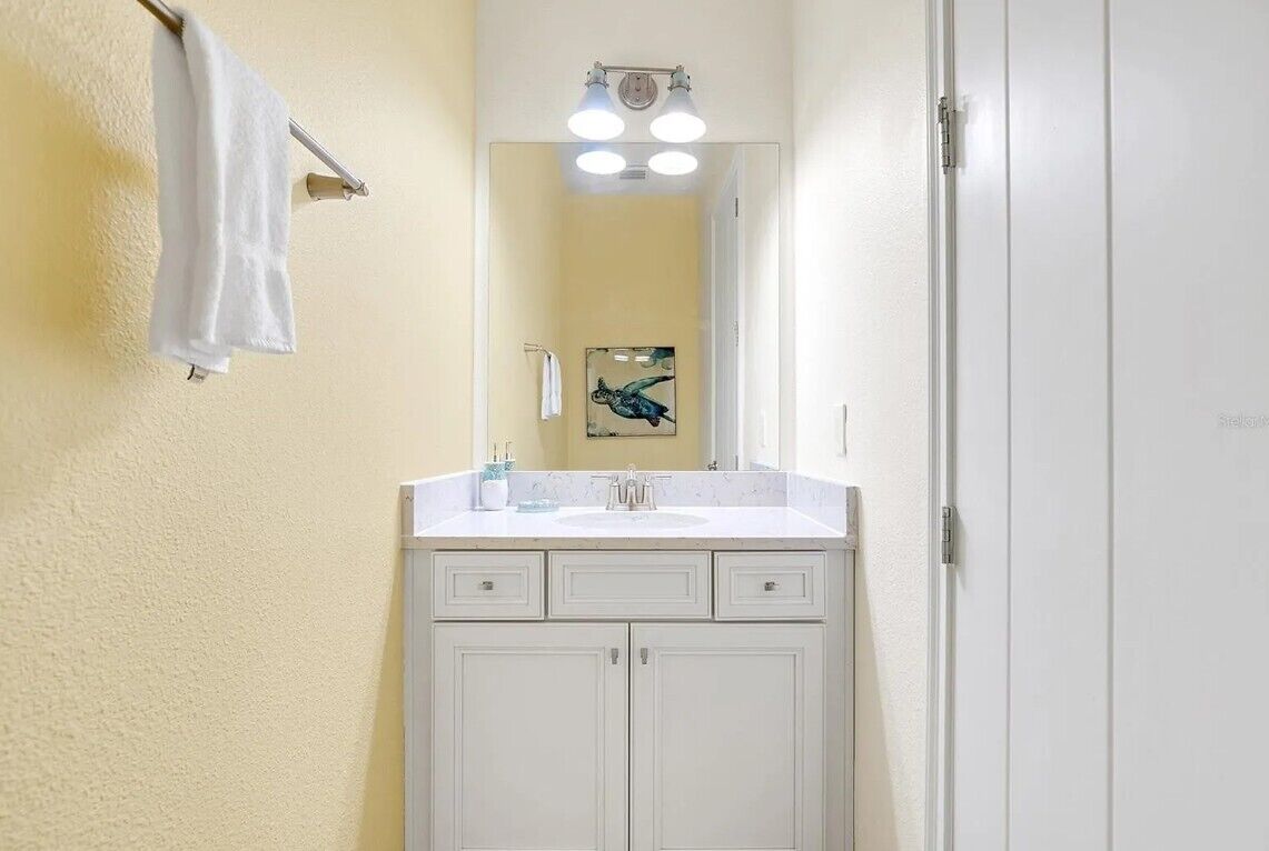 Un baño con un tocador blanco, un espejo y una toalla colgada en la pared.