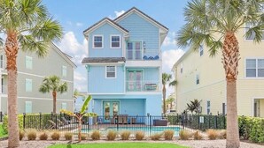 A two-story residential building with a balcony on the second floor, surrounded by palm trees and a fenced pool area.