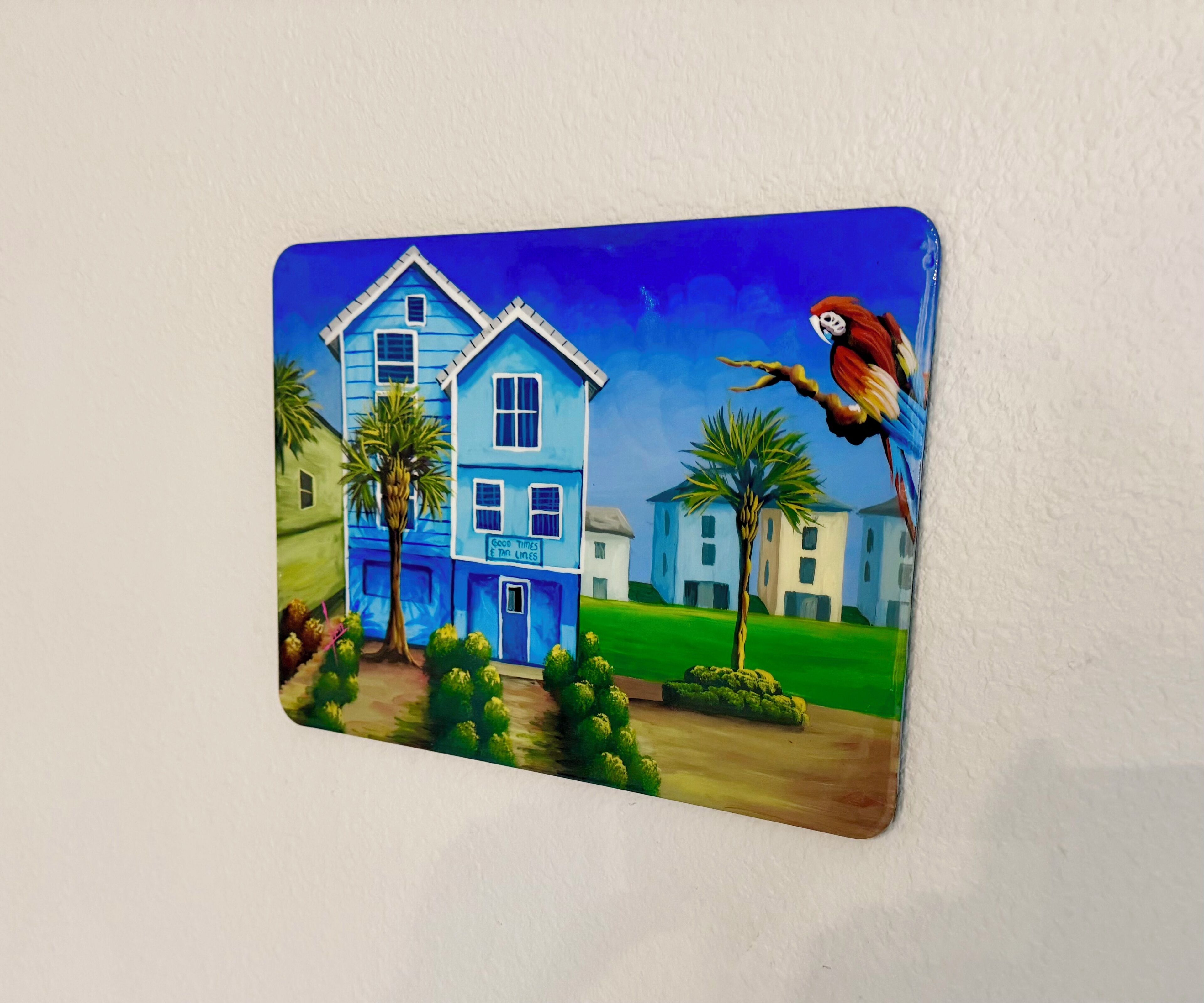 Une peinture colorée représentant une maison bleue avec un perroquet perché sur une branche.