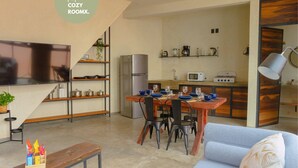 A modern living room with a sofa, a wooden coffee table, and a TV. There is a kitchen area with a refrigerator, microwave, and a dining table set for four. - Style & Comfort  A/C Loft + Terrace + Pets (Oaxaca de Juárez)