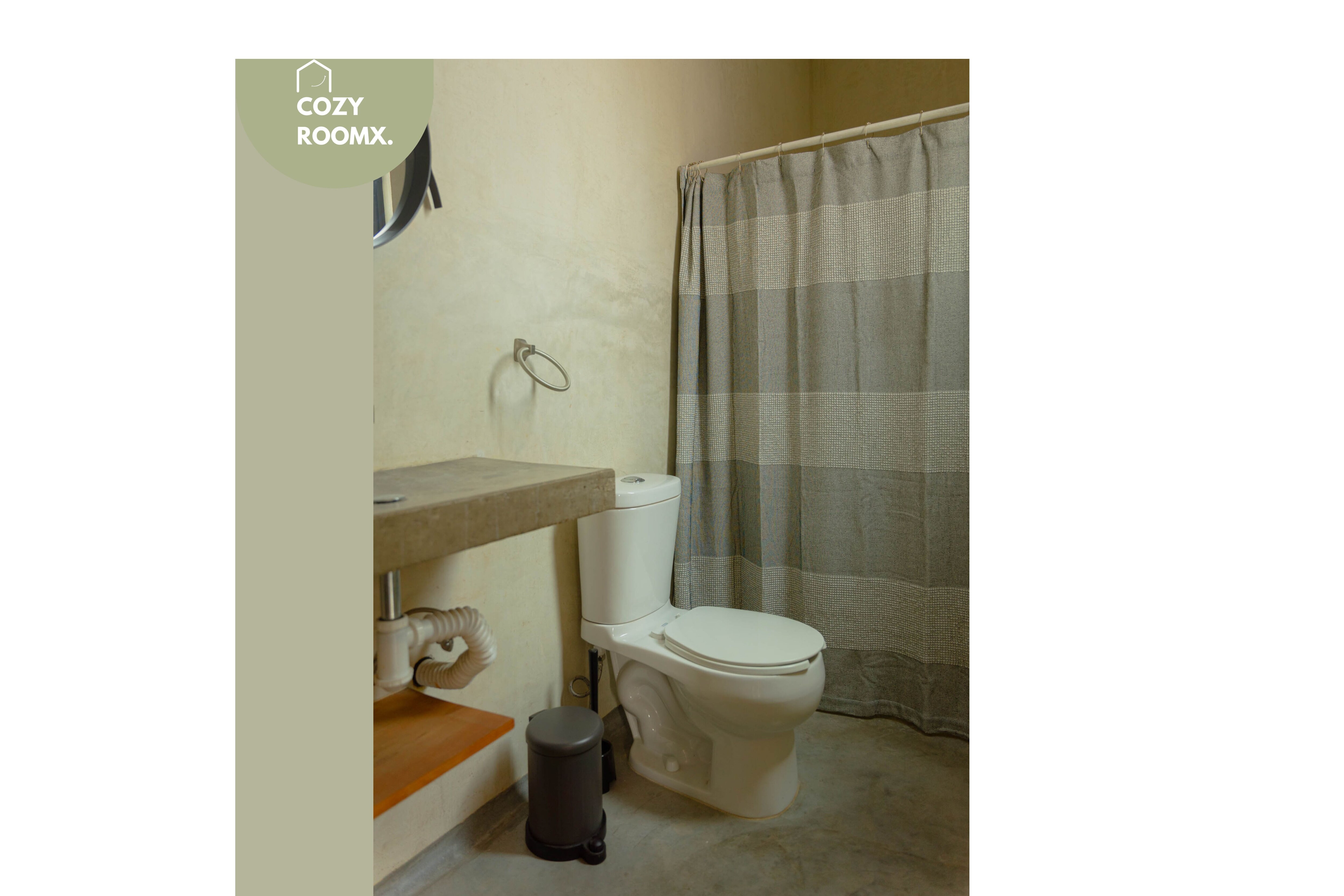 A bathroom with a toilet, a sink, a trash bin, and a shower curtain.