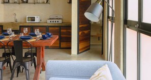 A cozy room with a dining table set for four, a sofa, a lamp, and a kitchen area with a microwave and coffee maker.