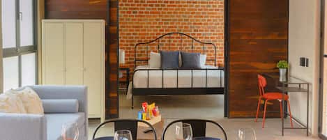 A modern room with a brick wall, a bed, a grey sofa, and a dining area with chairs and a table.