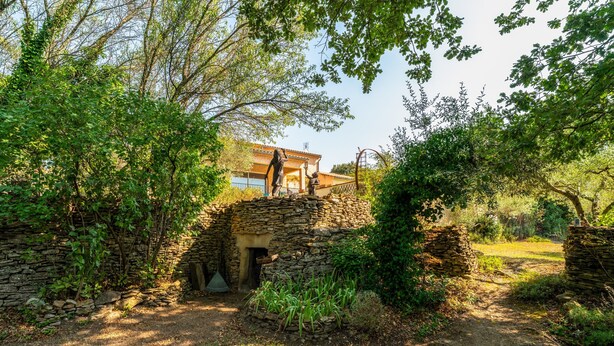 A stone structure with a doorway, surrounded by greenery and a building in the background. - Apartment 'Villabrix Near Uzès' with Wi-Fi (Vallabrix)