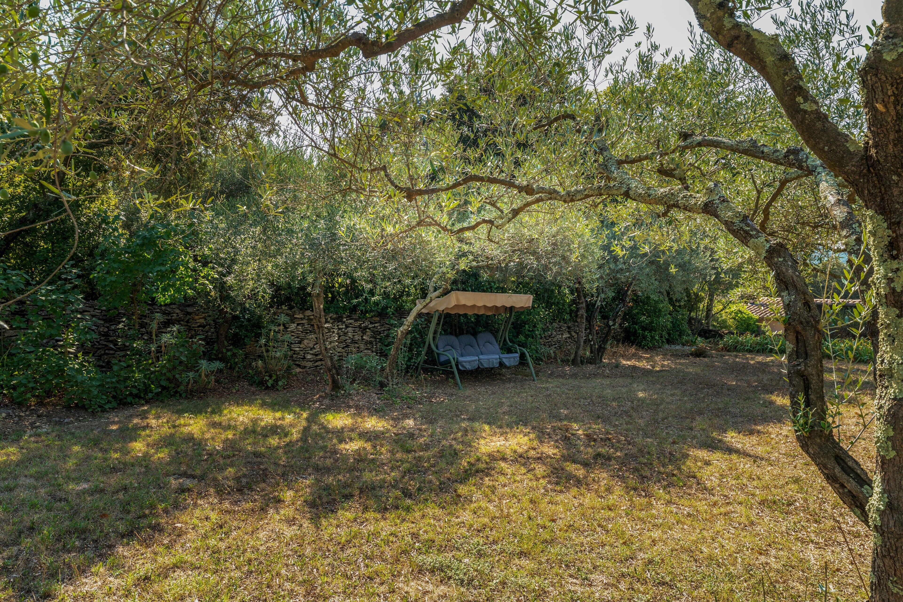 A secluded outdoor seating area with a rustic wooden table and chairs, surrounded by dense foliage and a stone wall.