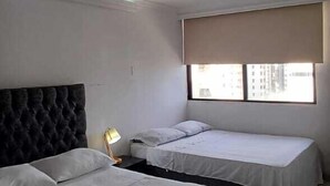 A hotel room with two beds, a dark headboard, a bedside lamp, and a window with a view of buildings. - APARTAMENTO 1105T (Cartagena)