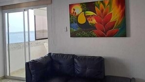 A spacious living room with a large window, a black leather sofa, and a colorful painting on the wall. - APARTAMENTO 1105T (Cartagena)
