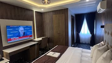 Una habitación de hotel moderna con una cama grande, un escritorio con computadora y un televisor mostrando noticias.