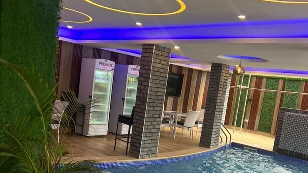 An indoor swimming pool with a tiled edge, surrounded by seating areas and a bar. - Presken Hotels Abuja (Abuja)