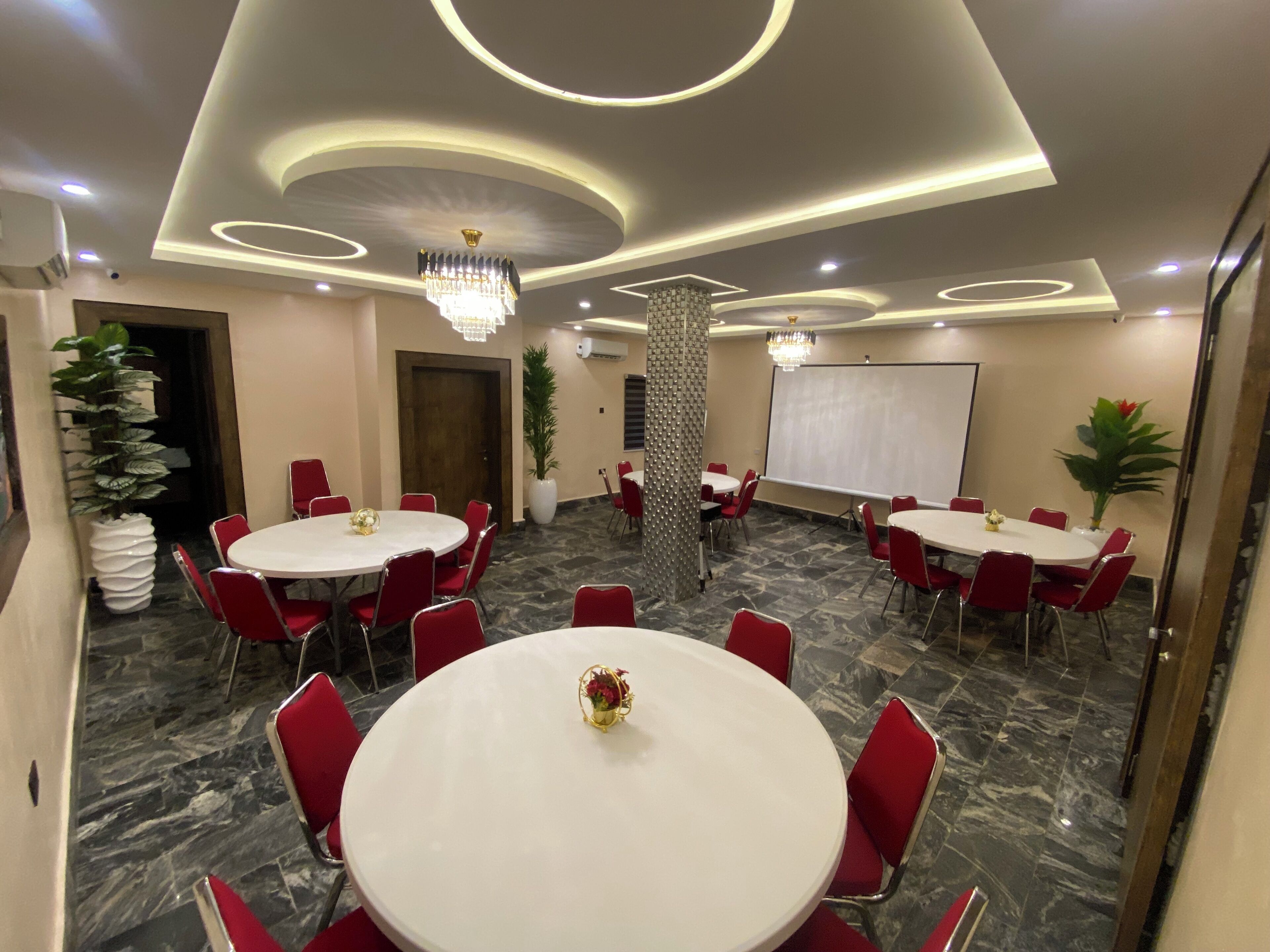 A conference room with multiple tables and chairs, a projector screen, and a decorative pillar.