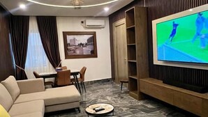 A modern living room with a sofa, two coffee tables, a TV, and a dining area. - Presken Hotels Abuja (Abuja)