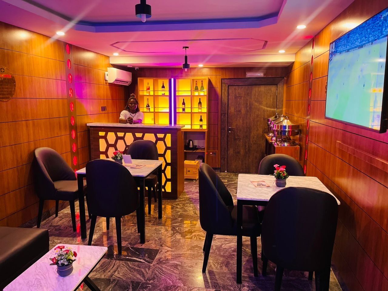 A restaurant with wooden paneling, a bar area, and a screen displaying a sports event.