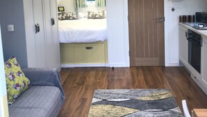 Una habitación funcional con cama, sofá, zona de cocina y una pequeña mesa de comedor.