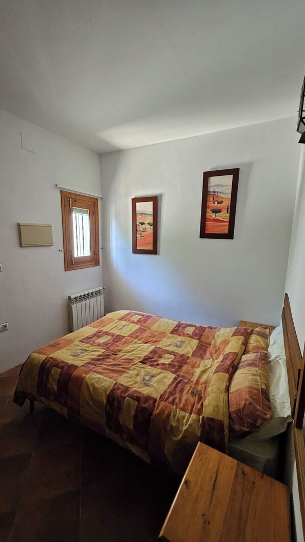 Un dormitorio con cama, ventana, radiador y dos cuadros en la pared.