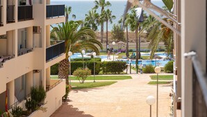 A hotel balcony with a view of a pool, palm trees, and the ocean. - 'Apartamento Zen Dreams Almerimar' with sea views, Wi-Fi, and air conditioning (Almerimar)