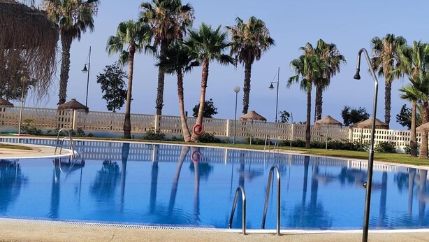 A swimming pool with palm trees and a fence in the background. - 'Apartamento Zen Dreams Almerimar' with sea views, Wi-Fi, and air conditioning (Almerimar)