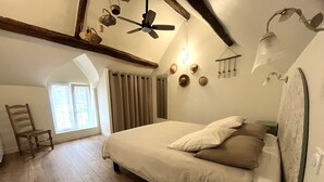 Une chambre à coucher avec un lit, une chaise, un ventilateur de plafond et une fenêtre.
