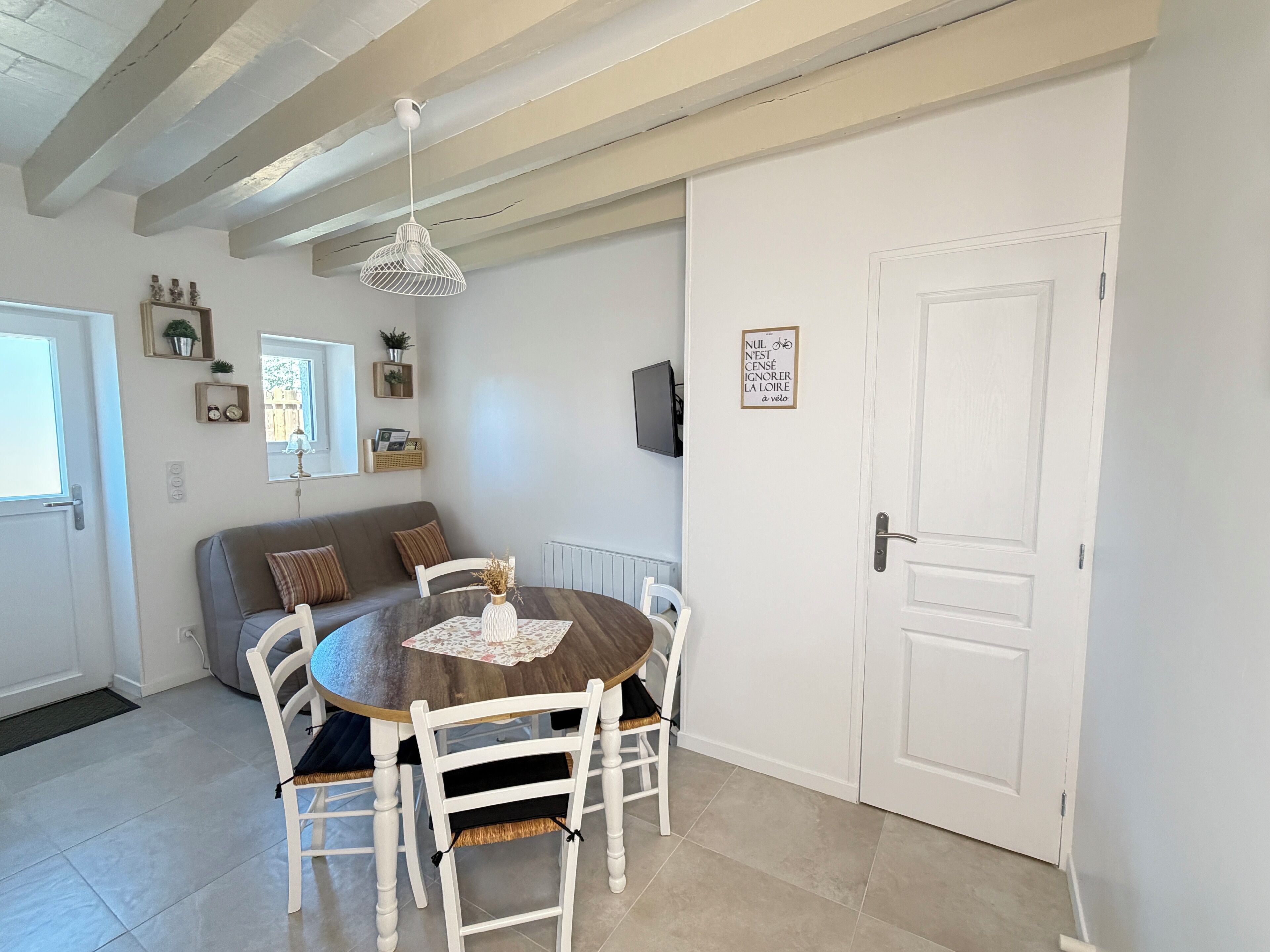 A dining area with a round table, white chairs, a hanging light fixture, and a white door with a sign.