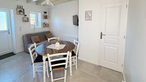 Un coin repas avec une table ronde, des chaises blanches, un luminaire suspendu et une porte blanche avec une enseigne.