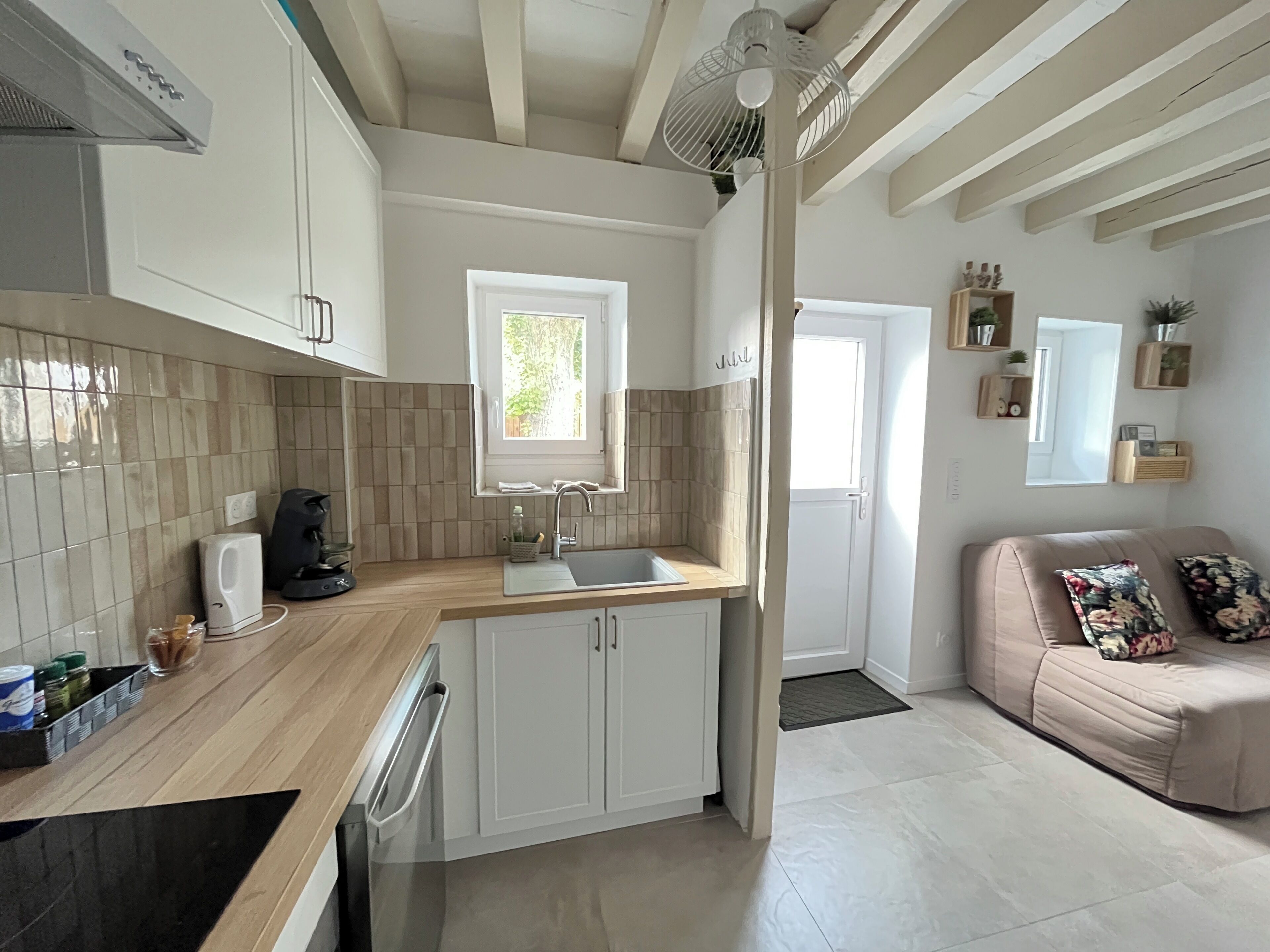 A modern kitchen with a window, white cabinets, a sink, and a coffee machine.
