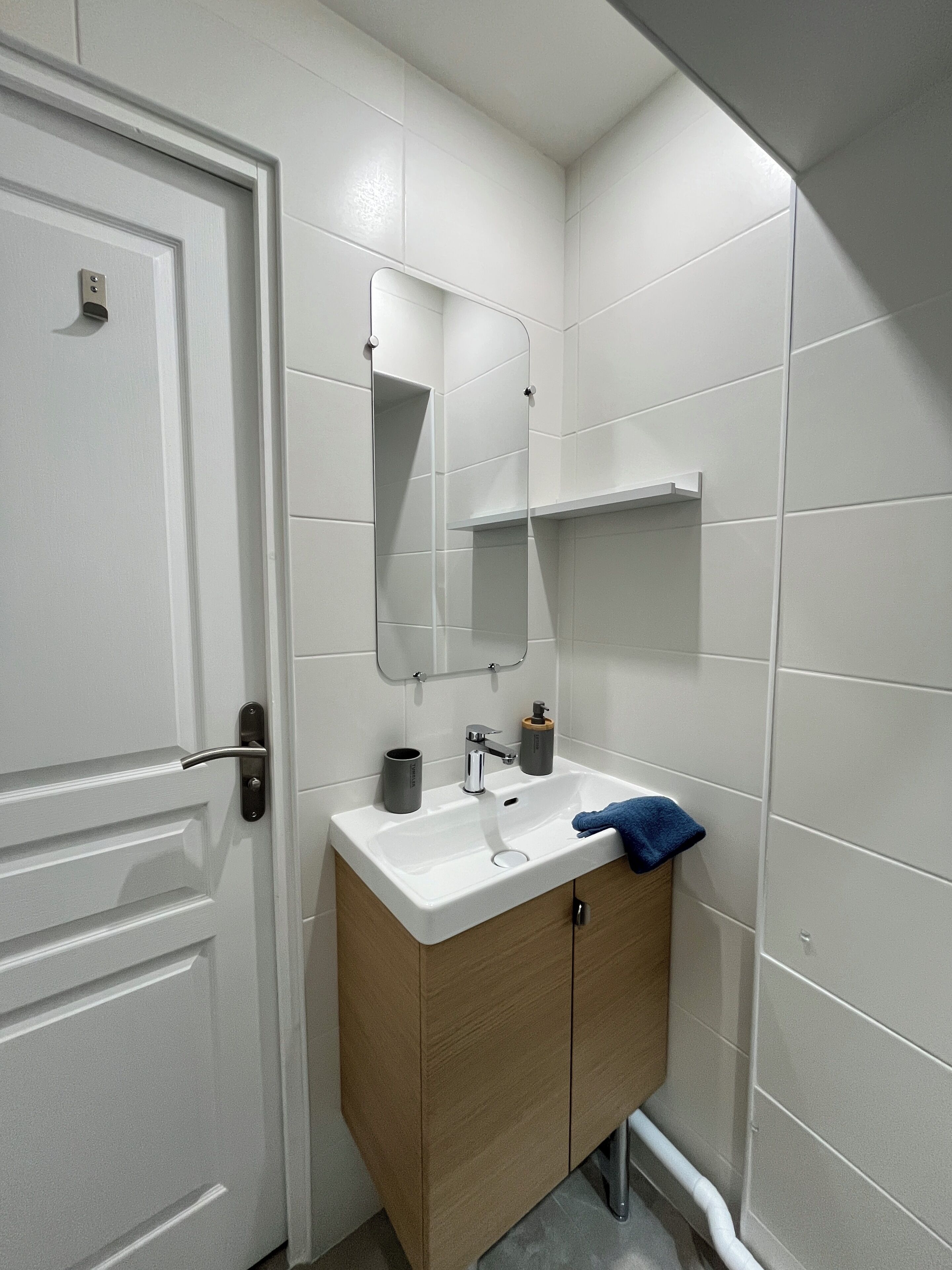 A bathroom with a white door, a sink with a mirror above it, and a towel hanging on the wall.