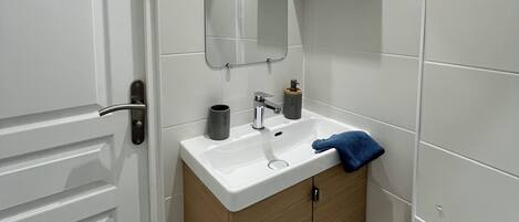 A bathroom with a white door, a sink with a mirror above it, and a towel hanging on the wall.