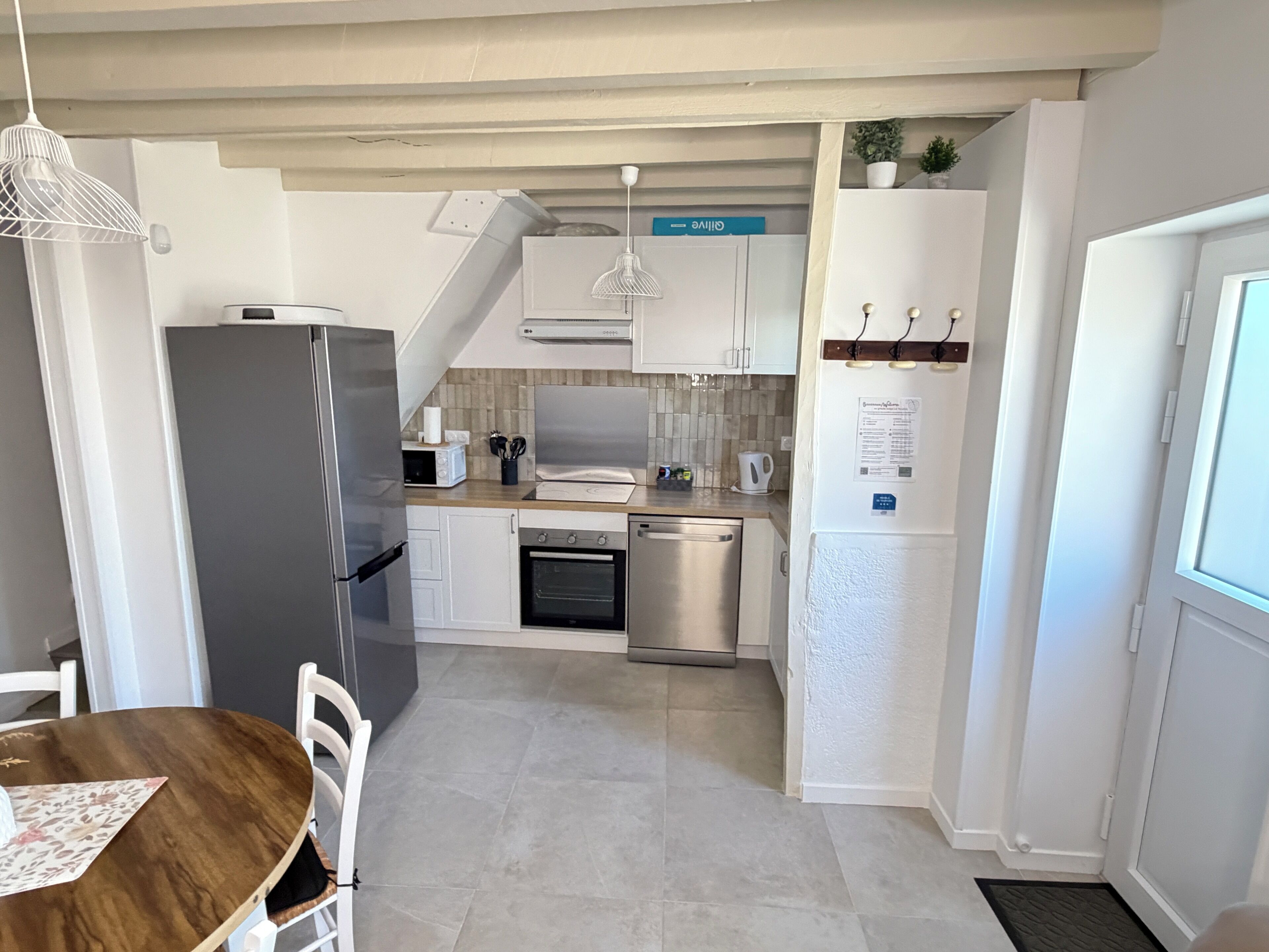 A compact kitchen with a refrigerator, stove, microwave, and sink. There is a dining table with chairs and a small plant on the counter.