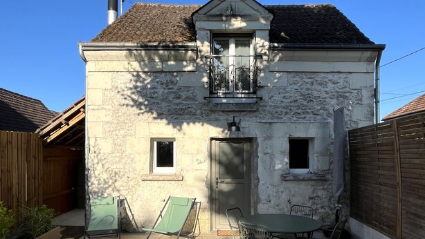Une maison en pierre avec un toit en tuiles, un balcon et une terrasse équipée d’une table et de chaises.