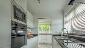 A modern kitchen with white cabinets, a built-in oven, a coffee maker, and a window with blinds.