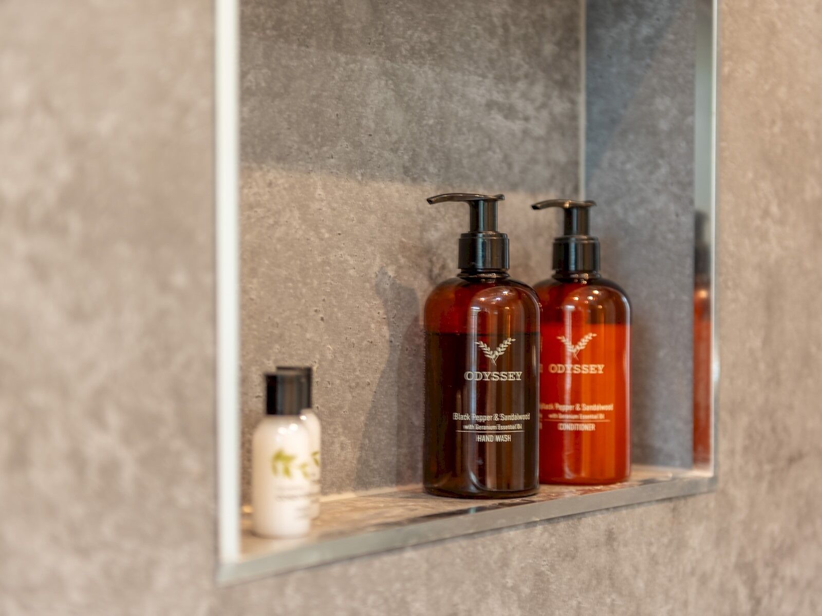 A bathroom shelf with two bottles of Odyssey Black Pepper & Sandalwood hand wash and a smaller bottle of a different brand.